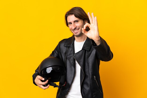 Photo man with a motorcycle helmet isolated on yellow showing ok sign with fingers