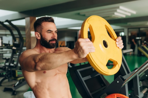 A man with a muscular torso holds weights in the gym