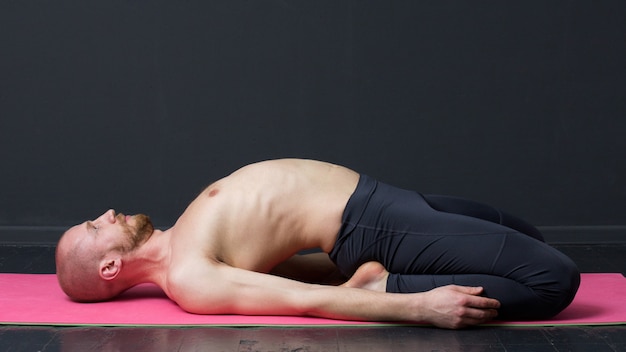 Man with naked torso is laying on the mat, bending the back