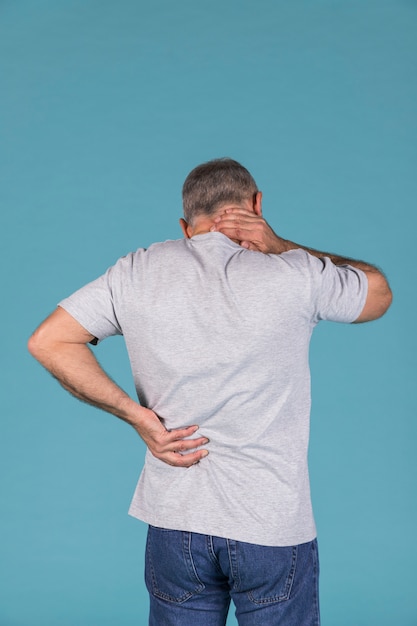 Man with neck and backache standing in front of blue backdrop