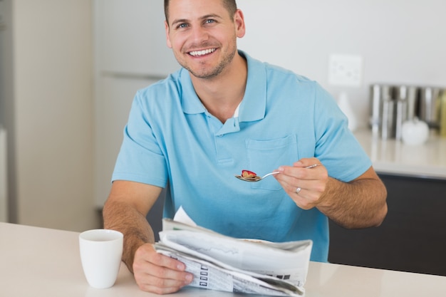 Man with newspaper having cereals at table