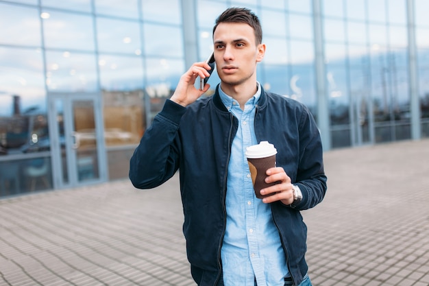 A man with a paper Cup of coffee, goes through the city, a handsome guy in stylish clothes, on the phone