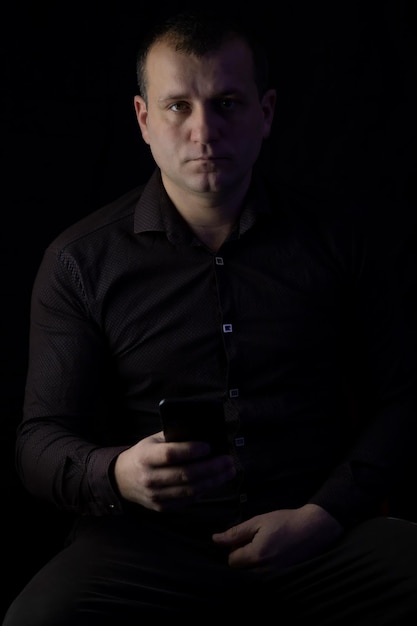 A man with a phone in a shirt on a black background