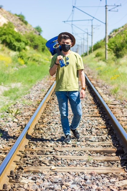 man with protective mask on railroad tracks playing on guitar