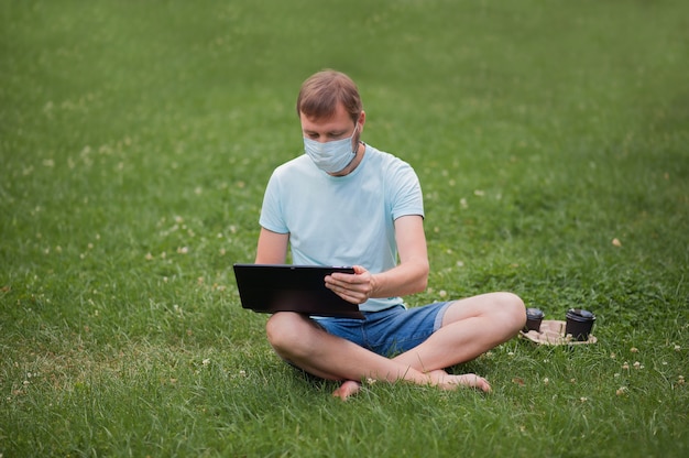 Man with a protective mask using a laptop in nature