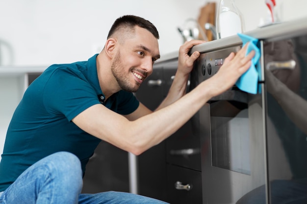 Photo man with rag cleaning oven door at home kitchen