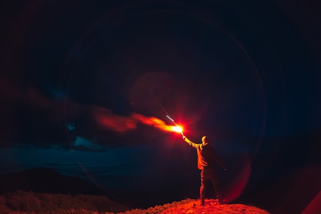 The man with a red firework stick standing on a night mountain