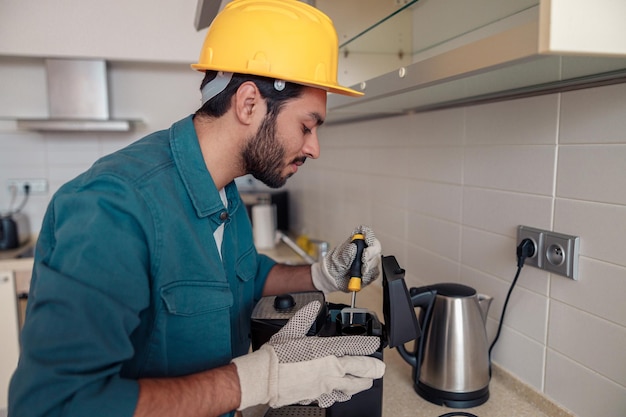 Man with screwdriver fixing coffee machine at table in kitchen maintenance and repair concept