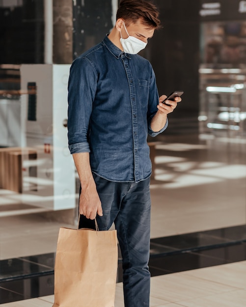 Man with a shopping bag reading a message on his smartphone. concept of health protection.