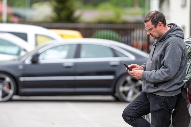 Man with smartphone standing next to the car using mobile app for paying car lock or Internet