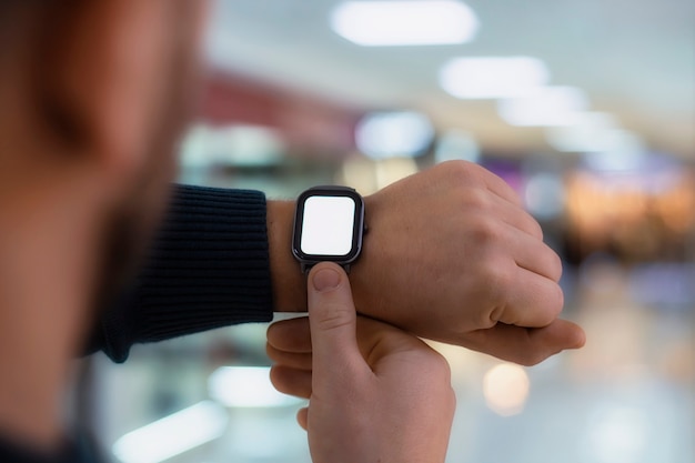 A man with a smartwatch and a white screen mockup on his hand. A man uses a fitness tracker on the background of a shopping mall.