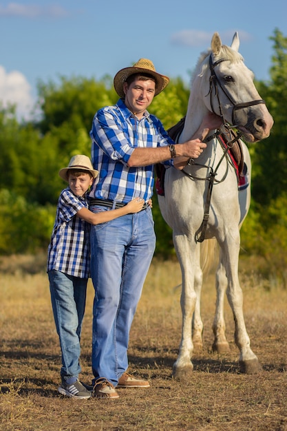 The man with the son in hats on walk with a white horse