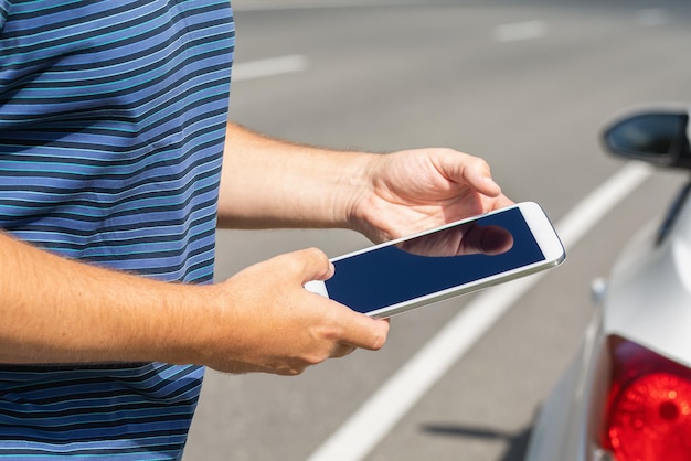 A man with a tablet on the road near the car finding a possible malfunction on the road