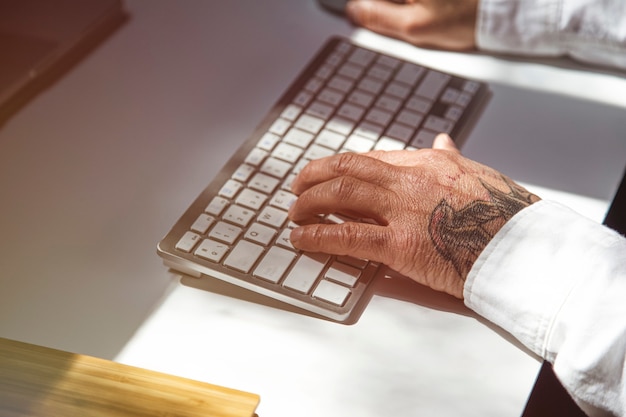 Man with tattoos browsing internet on laptop at office table