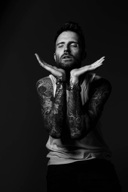 Photo a man with tattoos on his arms is sitting in a chair with his hands on his chest.