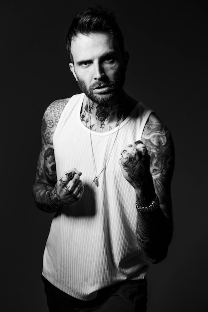 A man with tattoos on his arms is wearing a white tank top.