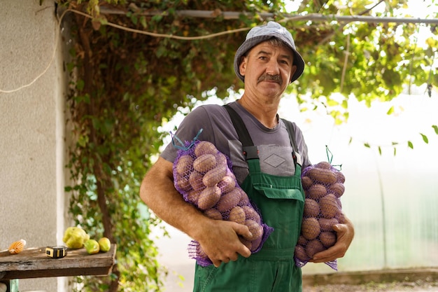 A man with two bags of potatoes Charismatic senior farmer holding sacks with potatoes