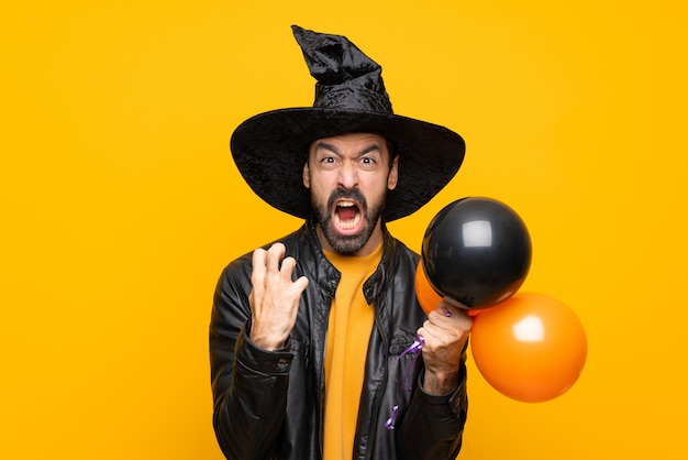 Man with witch hat holding black and orange air balloons for halloween party frustrated by a bad situation