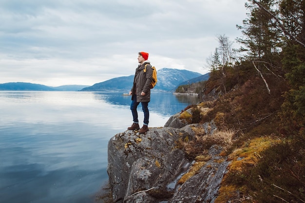 Man with a yellow backpack standing on a rock on background of mountain and lake