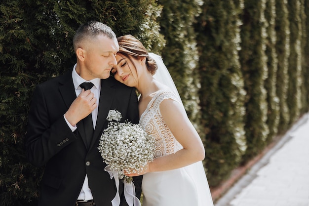 A man and a woman are hugging each other in front of a hedge