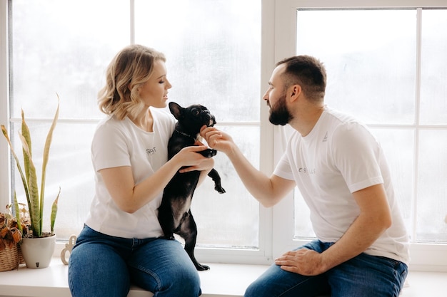 A man and woman are sitting in a window with a dog named bia.