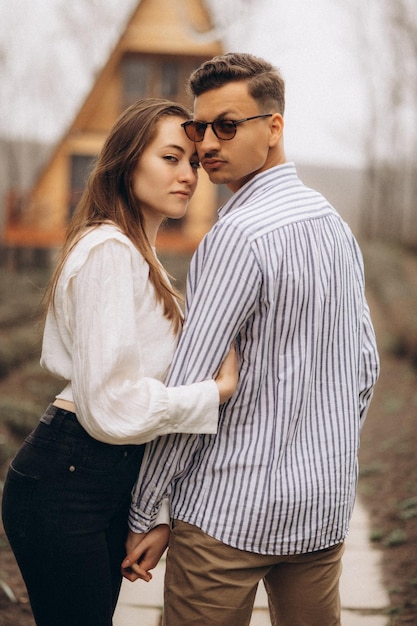 A man and a woman are standing together in front of a wooden house.