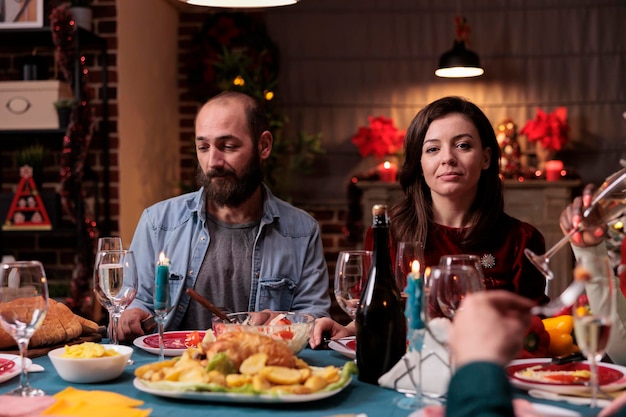 Man and woman celebrating christmas, sitting at festive dinner table, gathering at family home party. Friends eating home cooked xmas dishes in decorated beautiful place portrait