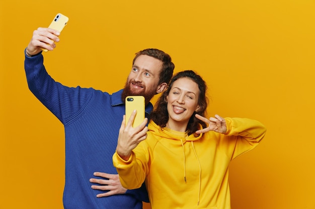 Photo man and woman couple smiling merrily with phone in hand social media viewing photos and videos on yellow background symbols signs and hand gestures family freelancers