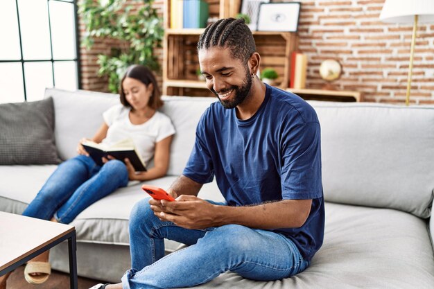 Man and woman couple using smartphone and reading book at home