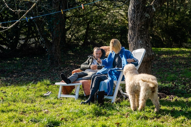 A man and a woman and a dog sit in the spring on sun loungers in the garden on green grass