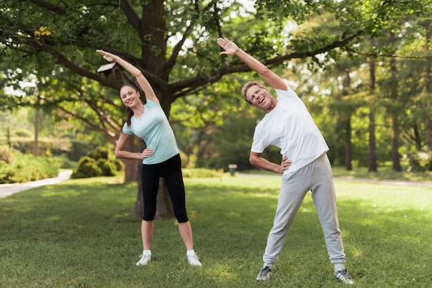 Man and woman doing exercises in the park. They warm up.