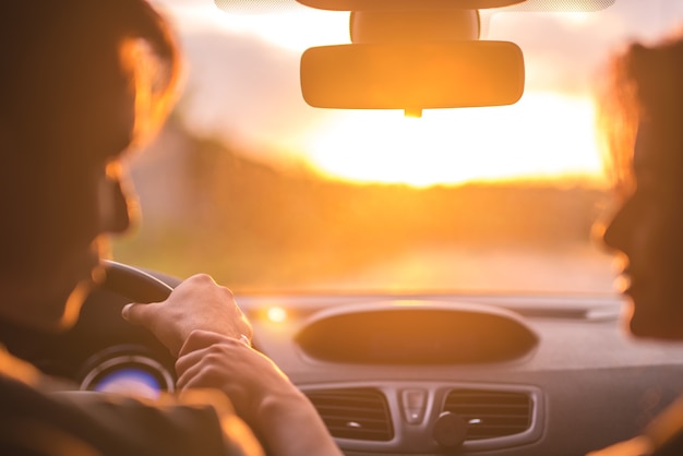 The man and woman drive a car on the background of the sunset