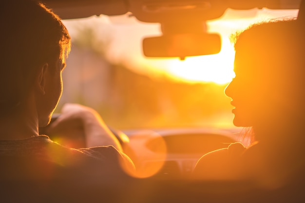 The man and woman drive a car on the background of the sunset