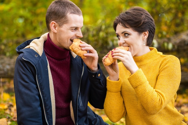 Man and woman eating croissants at autumn picnic