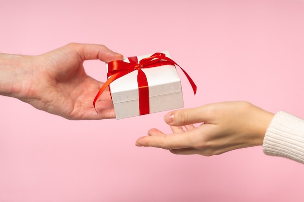 Man and Woman hands holding Valentine Gift on pink background