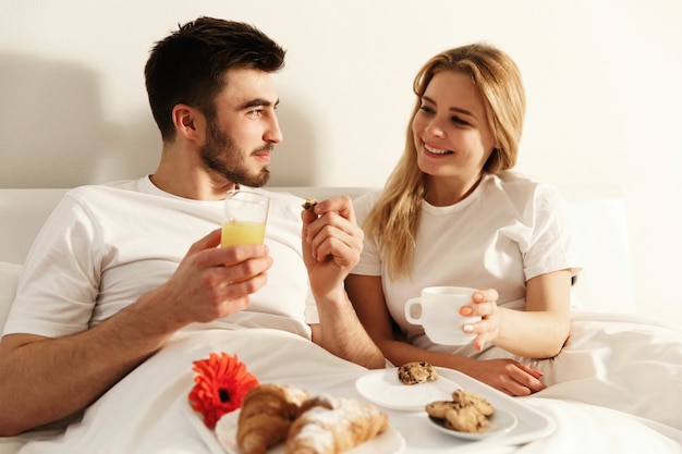 Man and woman have delicious french breakfast lying in the bed 