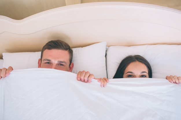 Man and woman hiding faces under white blanket