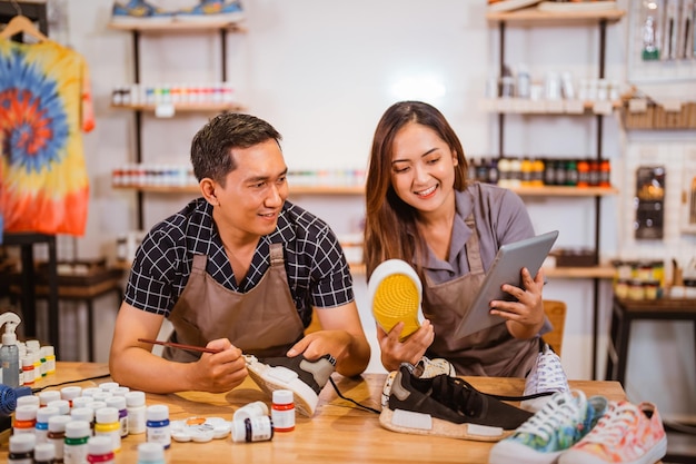 Photo man and woman holding tablet and sneakers shoes painting at workshop