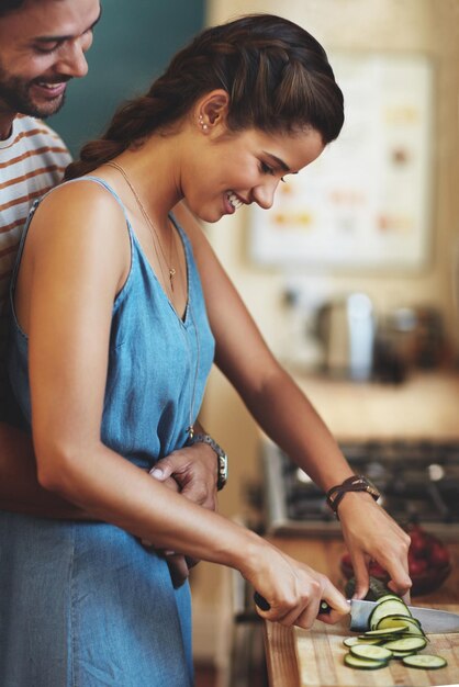 Man woman and hug with knife for cooking in kitchen care and diet with smile to prepare lunch in home Indian people happy couple and embrace with cucumber love and meal prep for dinner in house