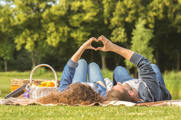 The man and woman lay on the grass and gesture love symbol