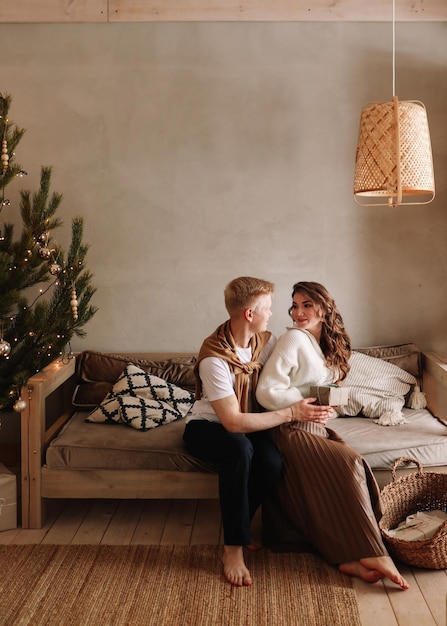 Photo a man and a woman in love embrace give gift gifts celebrate a holiday at the christmas tree at home