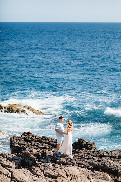 Man and woman in love stand embracing and holding hands on the rocky seashore