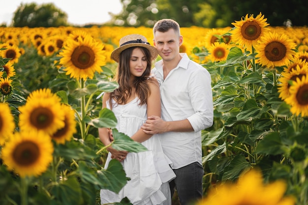 Man and woman in love standing in sunflower field during summer sunset.