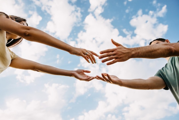 Man and woman reaching hands touching fingers on blue sky background