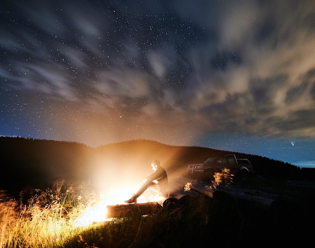 Man or woman relaxing and basking near cozy bonfire