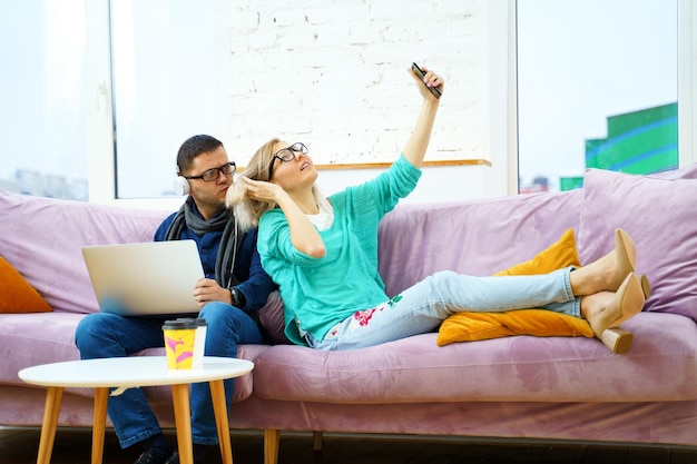 Man and woman sit on the couch chatting and using smartphone desktop computer