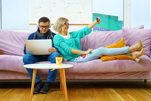 Man and woman sit on the couch chatting and using smartphone desktop computer