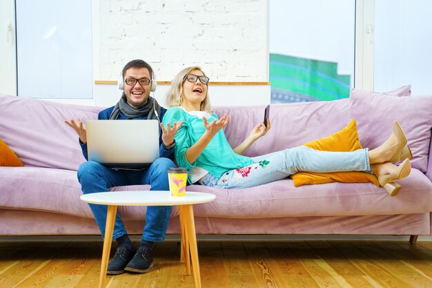 Man and woman sit on the couch chatting and using smartphone desktop computer