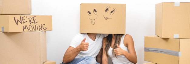 The man and woman sit on the floor with a carton box on the heads and gesture