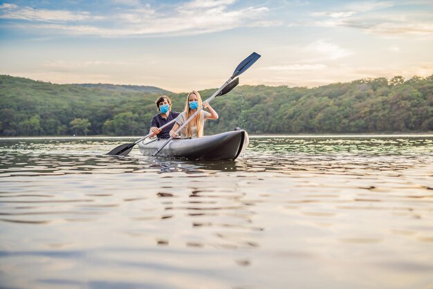 Man and woman swims on kayak wear medical masks due to the COVID19 coronavirus in the sea on background of island Kayaking conceptKayaking concept with family of father mother at sea